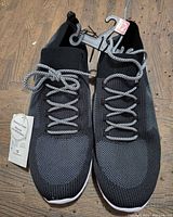 Top view of both shoes showing black knit upper and white patterned laces, with size 12 tag attached.