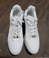 Front view of the pair of white MEXX sneakers showing lace-up design with gold accents on lace holders.
