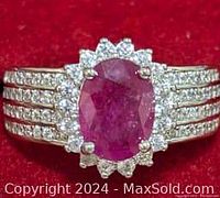 Close-up image of ring face showing oval ruby center with surrounding cubic zirconia stones and detailed band with CZ.