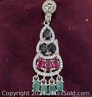 Sterling silver pendant displaying sapphire, emerald, and ruby stones on a dark fabric background