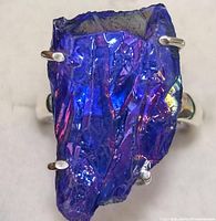 Close-up frontal image of ring showing large, irregularly shaped deep blue-purple iridescent gemstone set in stainless steel titanium prong setting.
