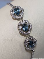 Close-up of the three blue topaz stones each surrounded by cubic zirconia in a flower-shaped setting on the sterling silver bracelet.
