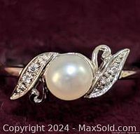 Close-up image of the ring's top view, showing the central white freshwater pearl with two leaf-shaped settings containing small clear stones on each side.