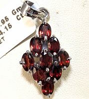 Close-up image of a sterling silver pendant with nine oval garnet gemstones in a cluster, attached to a polished silver bail.