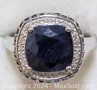 Close-up front view of the sterling silver ring with central dark blue sapphire surrounded by smaller clear stones on white background.