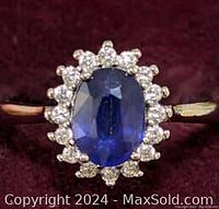 Top view of a sterling silver ring showing a large oval blue sapphire center stone surrounded by small round cubic zirconia stones on a velvet background.