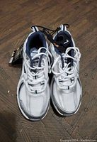 Top view of the white and navy blue women's running shoes with tags showing, placed on wooden surface.