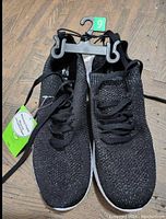 Pair of new women's size 9 black knit sneakers with white soles on a hanger, showing front and top view.