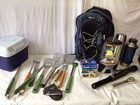 Photo of camping supplies including cooler, BBQ tools, backpack, lantern, flashlights, and thermoses