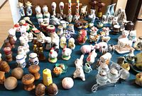 Wide view displaying a large variety of vintage salt and pepper shakers arranged on a blue surface, showing different materials like porcelain, wood, and glass in multiple shapes and colors.