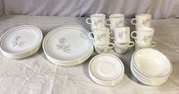 Photo showing stacks of dinner plates, medium plates, bowls, cups, and saucers with grey double stripe and rose design