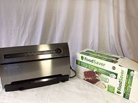 FoodSaver vacuum sealer and boxed accessories on white cloth background