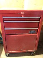 Front view of red Ford rolling metal tool chest showing three drawers and Ford emblem, with visible rust and stickers.