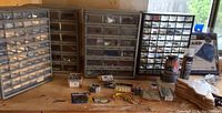 Wide view showing four multi-drawer hardware storage units and assorted hardware items on table.