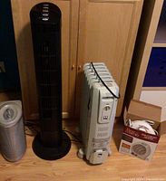 Four appliances grouped: DeLonghi radiator heater, Holmes black tower fan, small Holmes metallic barrel fan, boxed small compact fan heater