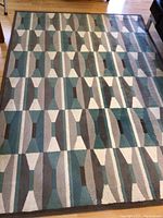 Geometric patterned rug in grey and teal tones laid out on floor.