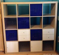 Front view of IKEA 4x4 cube storage rack with totes, drawers, and cabinet doors in blue, gray, and white.