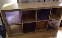 Full front view of the wooden cubed storage unit featuring 3 purple plastic cubes and 1 bark cloth cube in 8 cubbies.