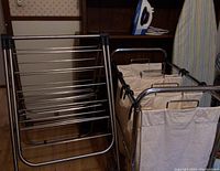 Photo showing folding metal drying rack and rolling laundry sorting cart with three cream canvas bags