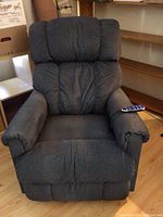 Front view of a blue/slate colored La-Z-Boy recliner with plush armrests, cushioned back made of fabric upholstery, and a remote resting on the right arm.
