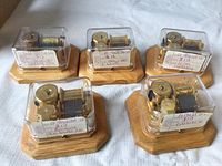 Photo of five music boxes mounted on wooden bases with clear plastic covers, each labeled with song titles.
