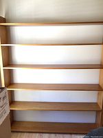 Front view of the oak bookcase showing five shelves against a white wall.