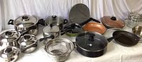 Full view of all cookware items: 5 Farberware pots with 4 lids, large Green Pan non-stick pan, 2 Gotham Pro pans, additional pots, lids, and strainer.