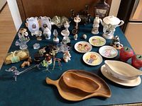 Overview of the entire collection showing porcelain, glass, and wooden small collectibles including figurines, plates, and trays arranged on a dark green fabric surface.