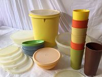 Rubbermaid kitchen items including bowls with lids, large yellow storage container, and colorful stacking drinking glasses