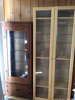 Full view of both wood display cabinets side by side showing their height, glass front doors, and overall build.