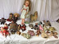 Wide view showing a large assortment of vintage dolls standing and lying down, with visible fabric and composite bodies in various dress styles.