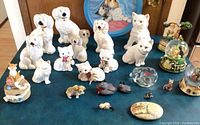Full layout of 27 items on blue tablecloth, showing porcelain cats and dogs, small figurines, painted rocks, music boxes, and decorative items