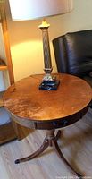 Full top view of round wooden small table with vintage table lamp on it, showing surface wear and drawer