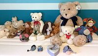 Full grouping of vintage teddy bears and other plush animals on a white shelf with a blue background. Includes Tigger, Eeyore, and various teddy bears.