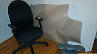 Black adjustable office chair next to beige floor protector mat and gray foot rest on hardwood floor.