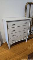 Front view of vintage 4-drawer white painted dresser with metal handles, showing overall shape and condition.