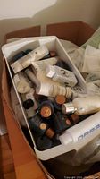 Close-up of bin filled with assorted hotel-sized bottles of shampoo, conditioner, lotion, and other personal care liquids, plus small combs and soaps.