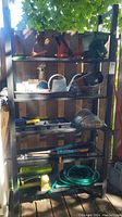 Full view of metal shelving unit holding garden tools such as a Black & Decker 16" trimmer, garden snips, hose, sprinklers, watering can.