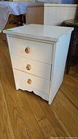 Front view of the white painted wood 3-drawer night stand showing round wooden knobs and visible wear on edges.