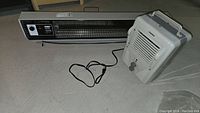 Photo showing both Seabreeze two heat automatic heater and NomaUH-1509 heater on floor with cords visible