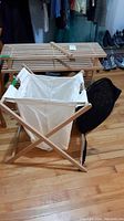 Photo of wooden slat racks with white laundry bag and wooden holder in front and black mesh laundry bag on floor