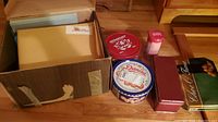 Box with large beige album and multiple tins arranged on floor