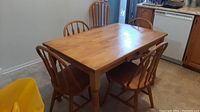 Rectangular wood table with four chairs around it and one chair at side in kitchen setting