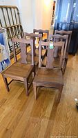 View of six vintage teak wood dining chairs arranged in two rows showing their distinct carved back design and seat area.