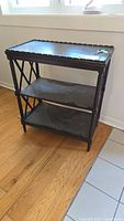 Front angled view of the vintage dark wood display side table showing top with scalloped edge, two shelves, and decorative side panels.