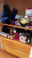 Shelf display of winter gloves, mitts, scarves, vests, stuffed toys including a Harrods bear and monkey, and winter hats