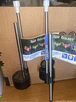 Two Alpine Solaris solar garden stakes with black bases and white light diffusers, one with a dragonfly decoration attached; packaging label visible