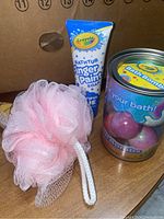 Photo showing Crayola Finger Paint Soap, pink mesh bath sponge, and container of bath bombs with colorful spheres.