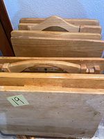 Seven wooden folding TV trays nested together showing top edges and handles. Natural wood finish with some visible use marks.