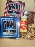 Photo showing Lakeshore giant red and blue sealed ink pads, Classic brush-on red stamp ink bottle, and two Christmas-themed wooden stamp blocks